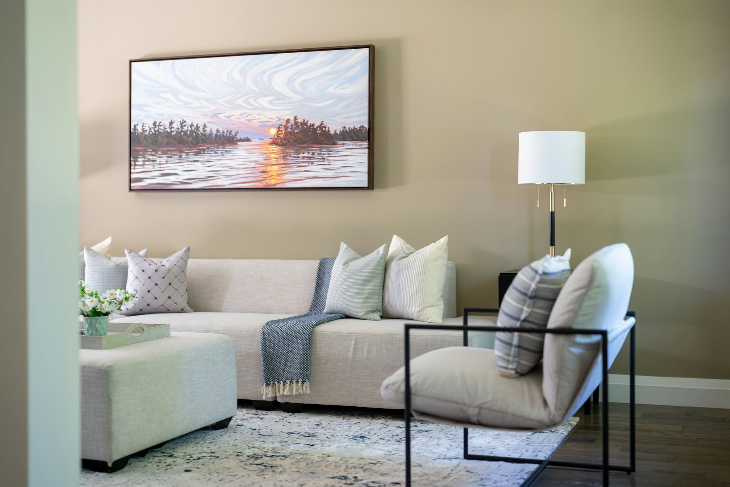 Sunset lake landscape print above a sectional sofa in a warm, sunlit living room