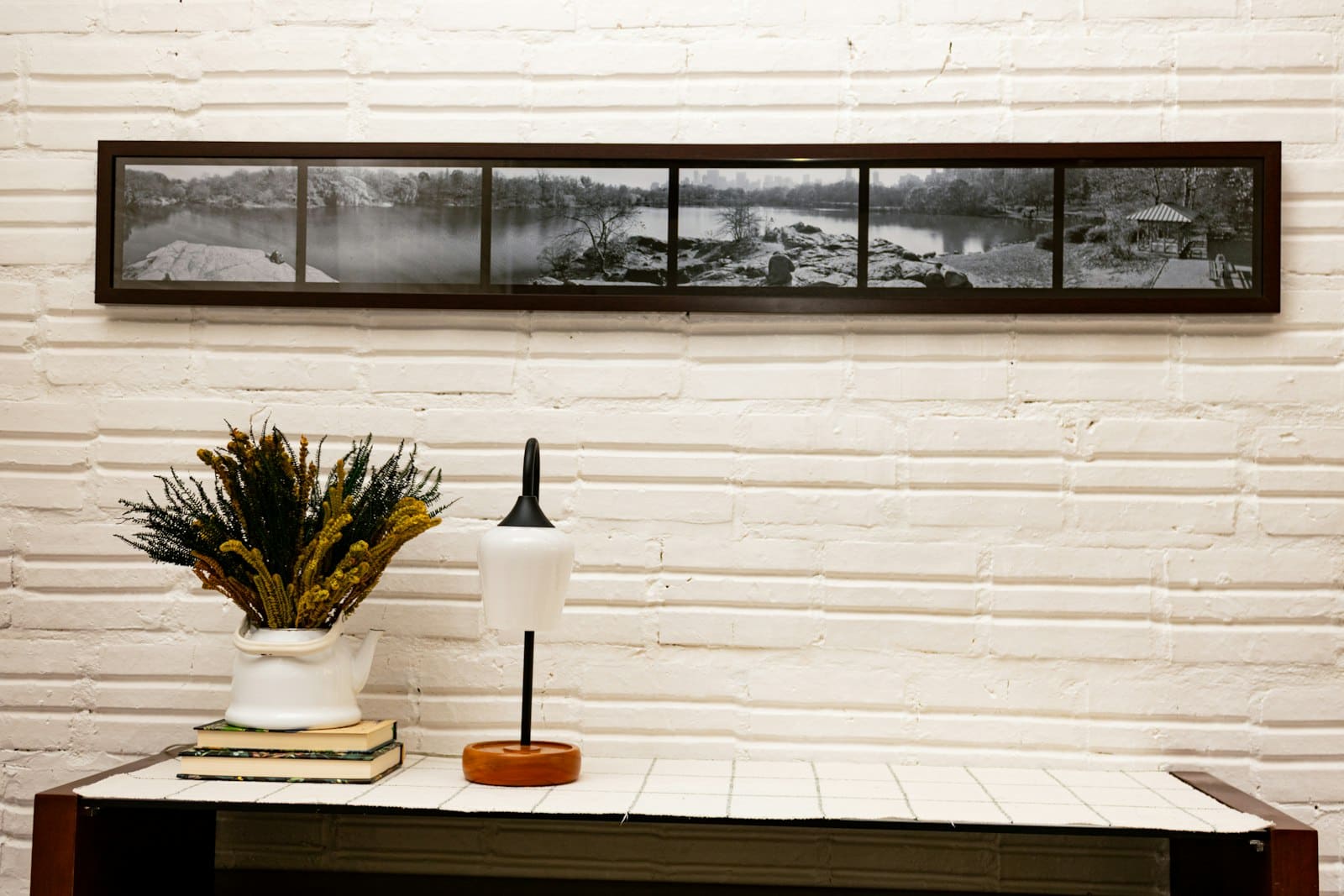 Panoramic black-and-white landscape print in a dark frame above a rustic console