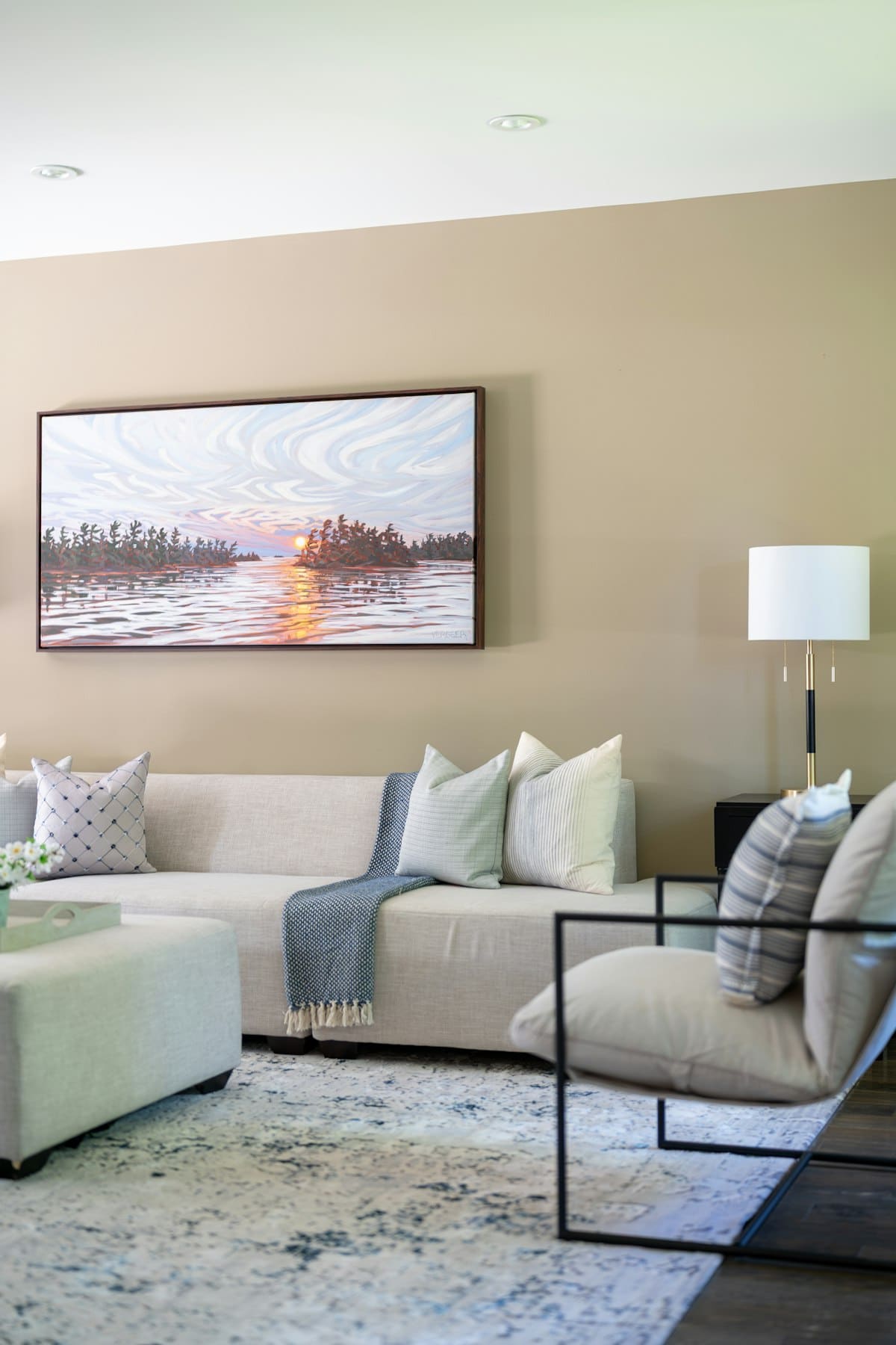 Sunset lake landscape painting above a light sofa in a warm living room