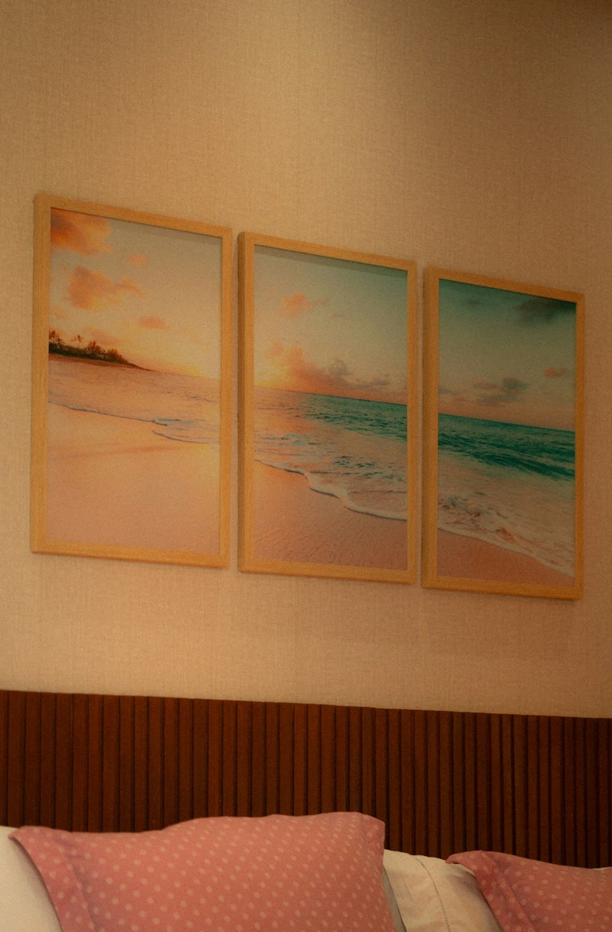 Three warm sunset seascape prints in wood frames above a bed